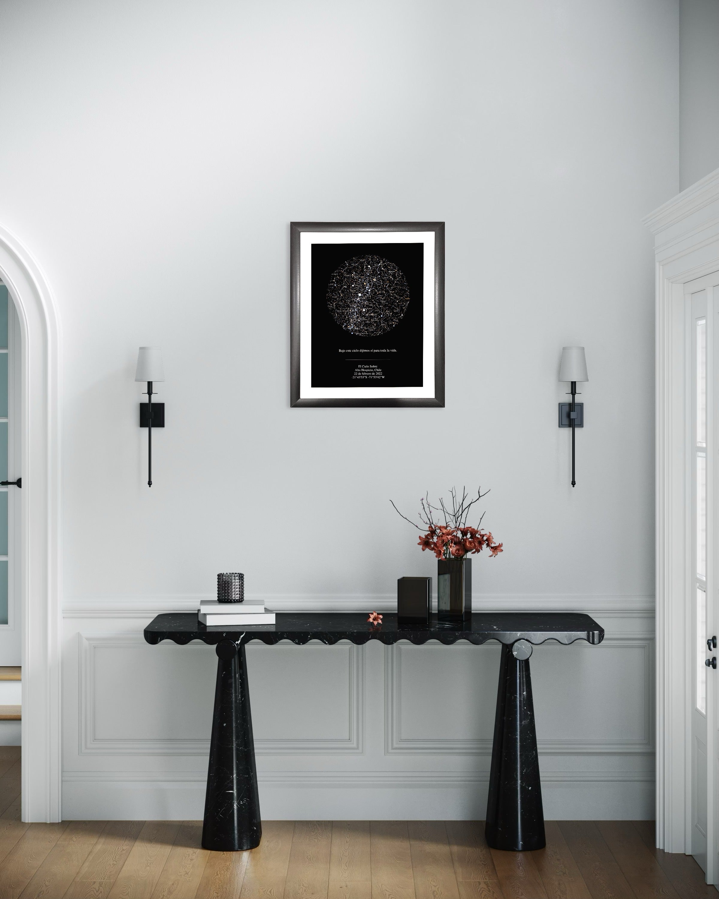 Mapa estelar XXL enmarcado sobre consola negra en recibidor elegante de pared blanca