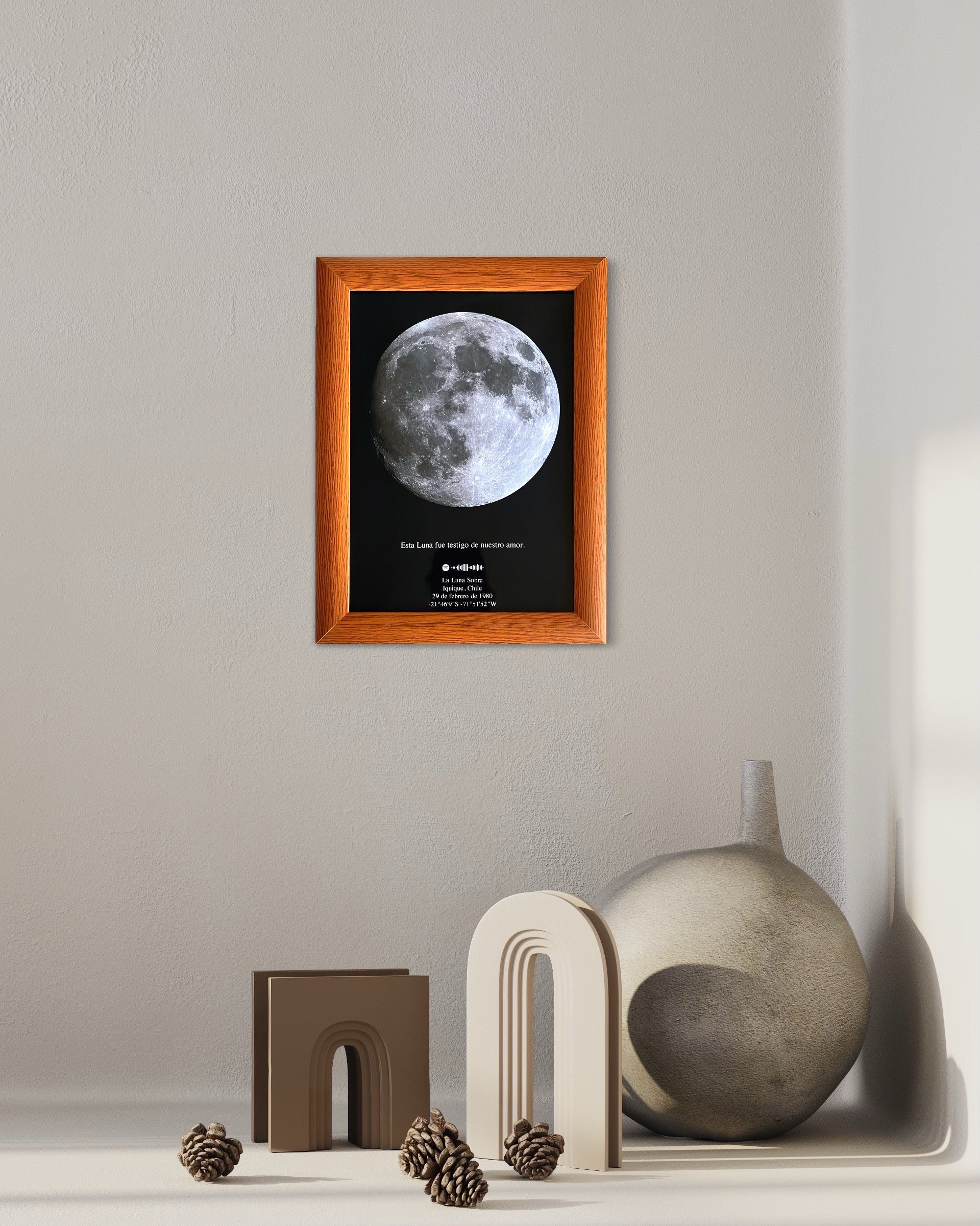 Mapa lunar enmarcado con borde de madera color miel colgado sobre una repisa decorativa con jarrón y figuras modernas.