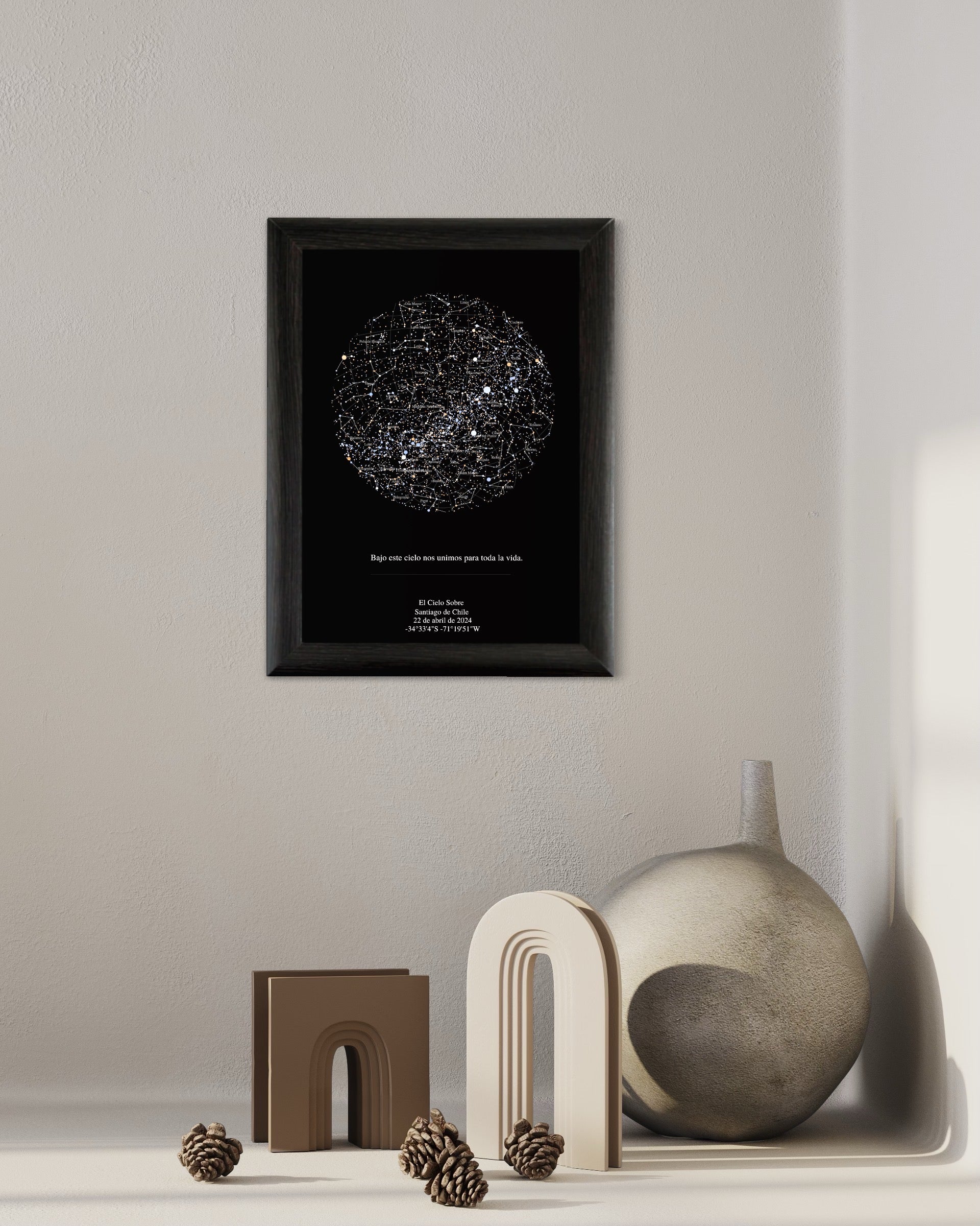 Cuadro Mapa Estelar Sky of Colors en marco negro sobre repisa minimalista beige, junto a figuras decorativas en tonos arena.