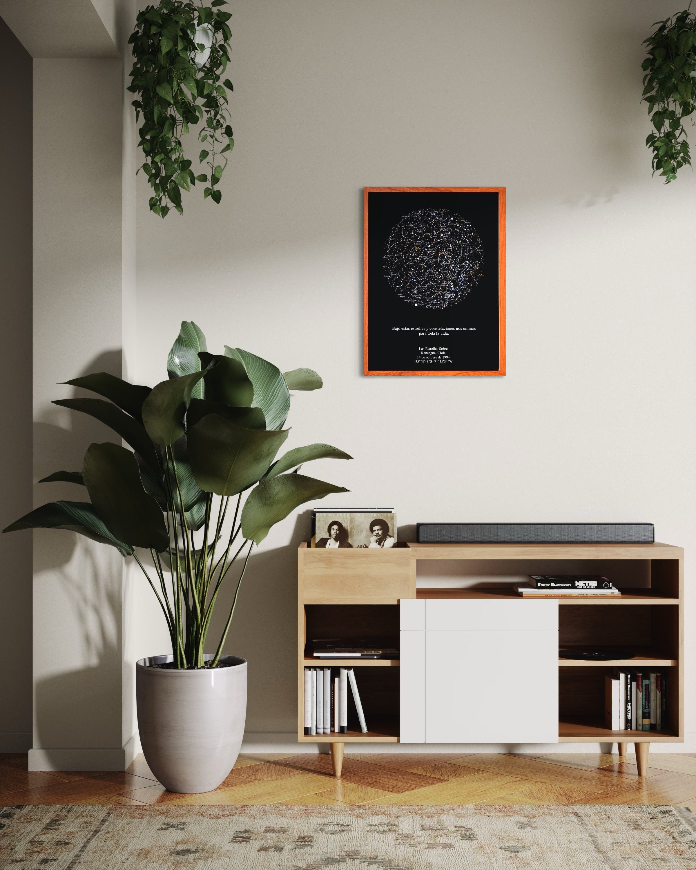 Mapa estelar para parejas con fondo negro y marco color madera colgado sobre un aparador de madera en un living moderno con planta grande decorativa.