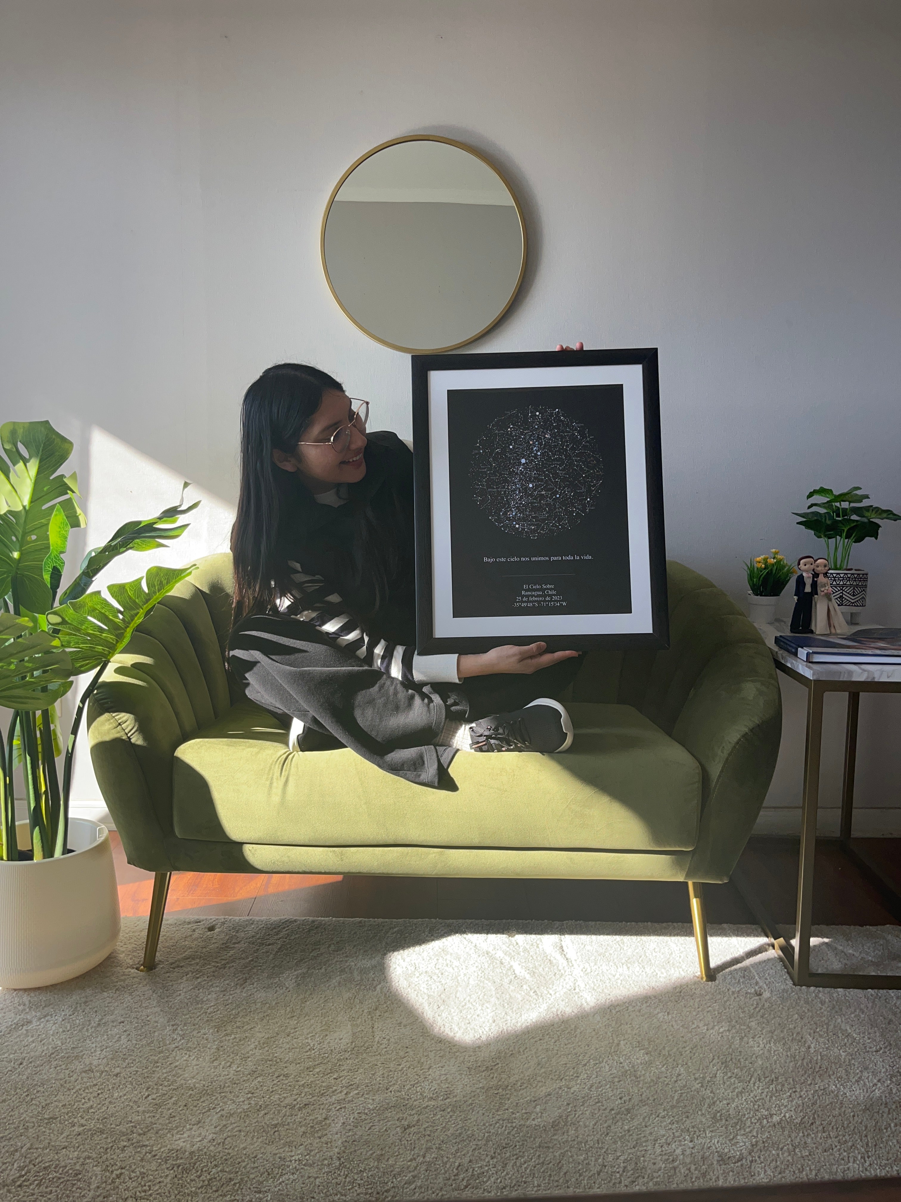 Mapa estelar XXL en marco negro con paspartú blanco sostenido por mujer en living iluminado