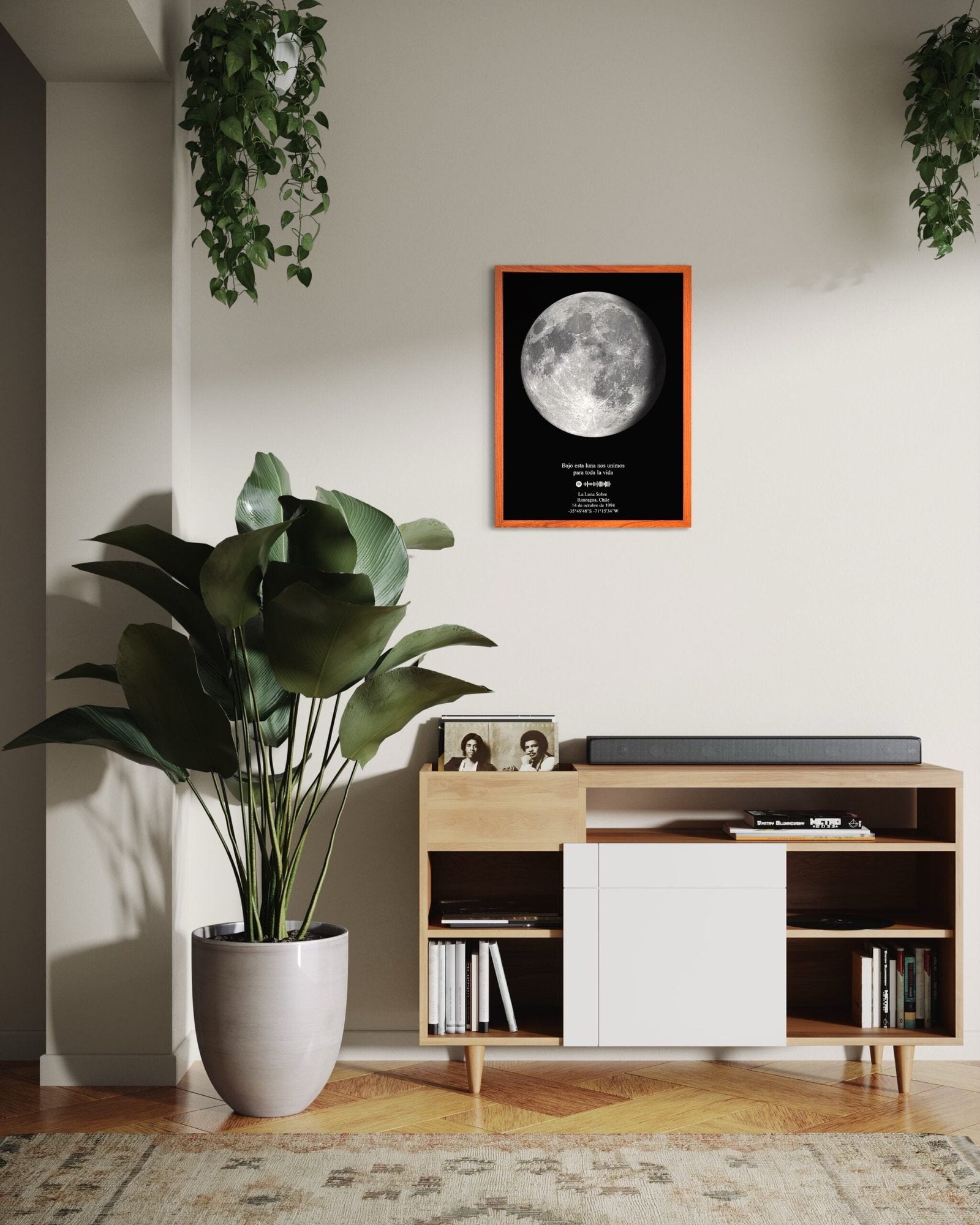 Cuadro Mapa Lunar XL enmarcado sobre un mueble de madera claro, decorado con planta grande y fotos familiares en un living acogedor.