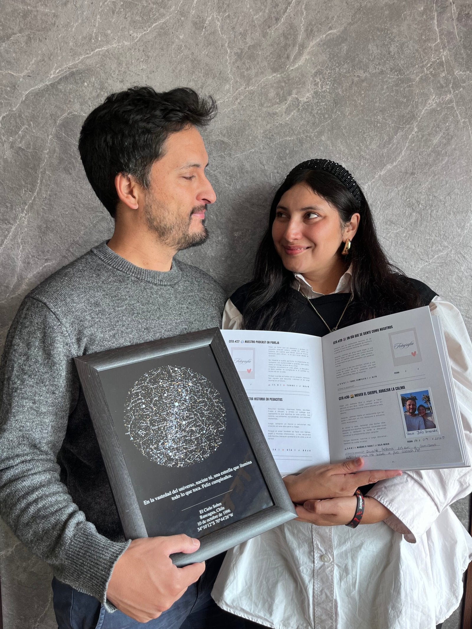 Pareja de pie mirando sus ojos mientras sostiene el Álbum para Parejas "Esto va en serio" abierto y un Mapa Estelar Sky of Colors enmarcado.