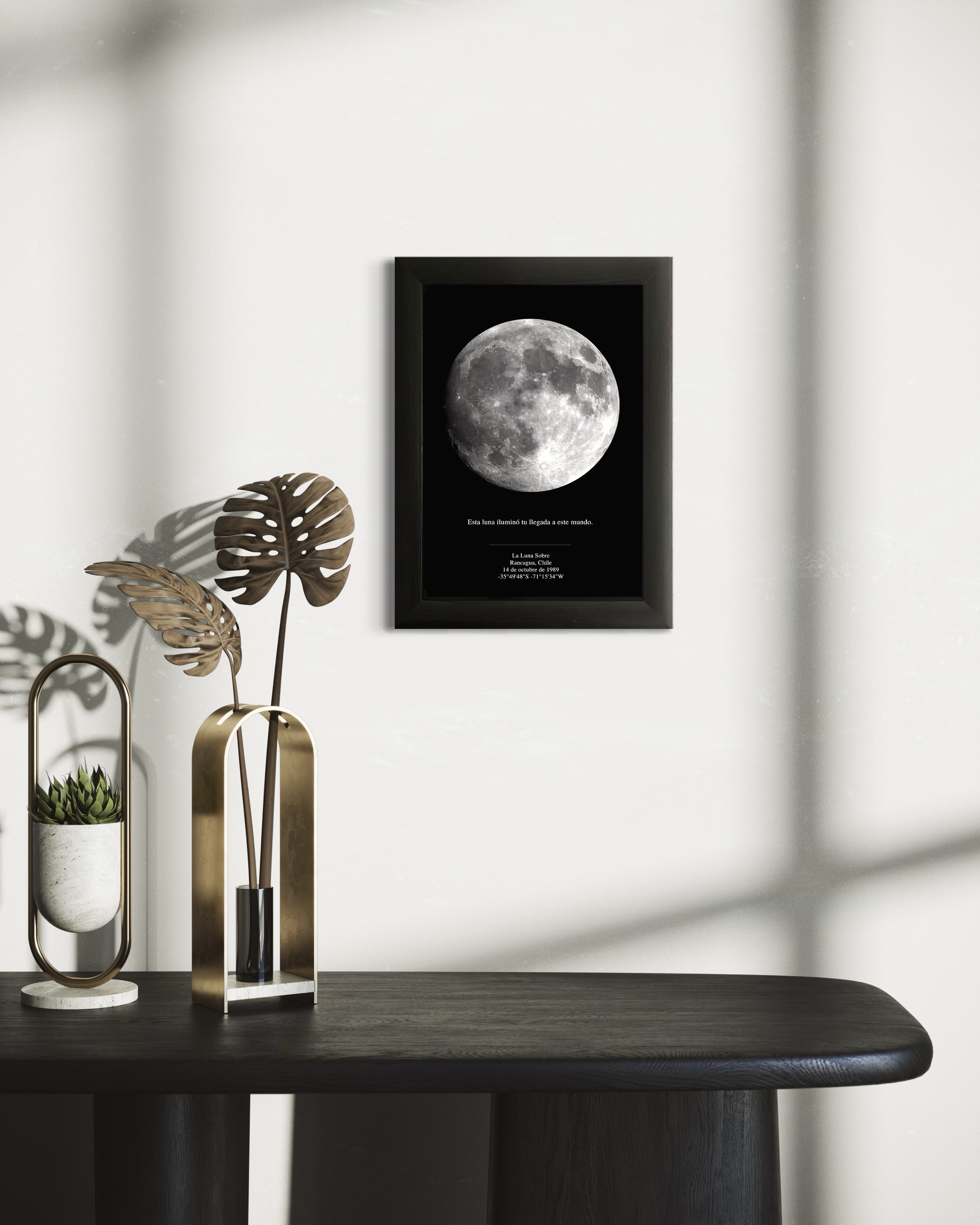 Mapa lunar enmarcado en negro decorando una pared minimalista, acompañado de jarrones dorados y plantas, ideal como cuadro moderno para el hogar.