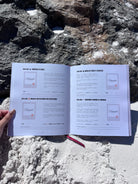 Álbum para parejas “Esto va en serio” abierto sobre la arena en la playa, mostrando sus páginas interiores con citas guiadas y espacios para escribir recuerdos.