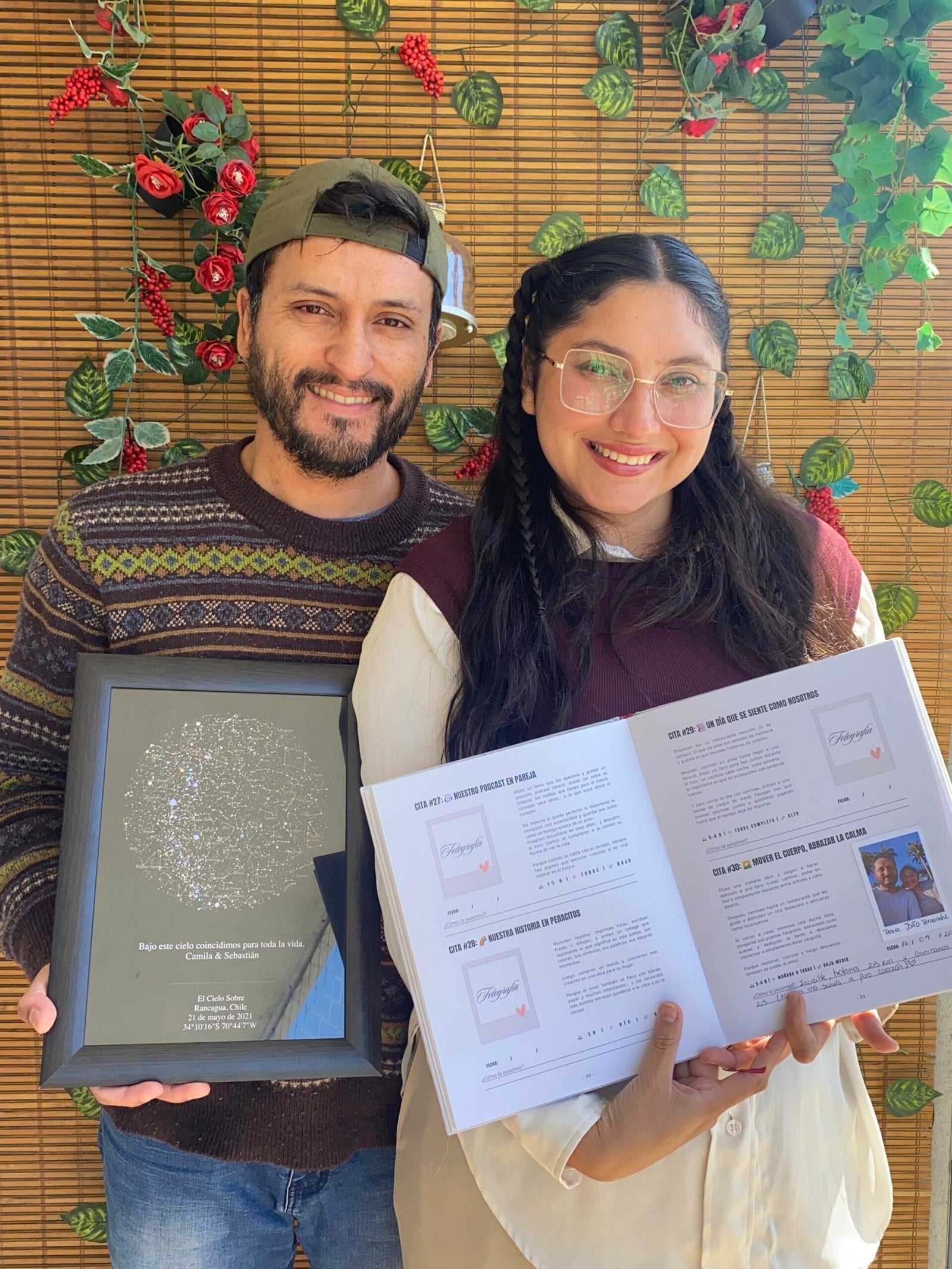 Pareja sonriendo mientras sostiene el Álbum para Parejas "Esto va en serio" abierto y un Mapa Estelar Sky of Colors en marco negro.