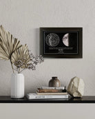 Mapa estelar con la fase lunar exacta de una fecha especial, enmarcado en negro sobre mesa decorativa de estilo moderno