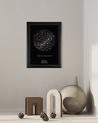 Cuadro Mapa Estelar Sky of Colors en marco negro sobre repisa minimalista beige, junto a figuras decorativas en tonos arena.