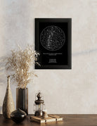 Cuadro negro con mapa estelar personalizado colgado sobre una mesa con jarrones decorativos y ramas secas en un ambiente minimalista y cálido.