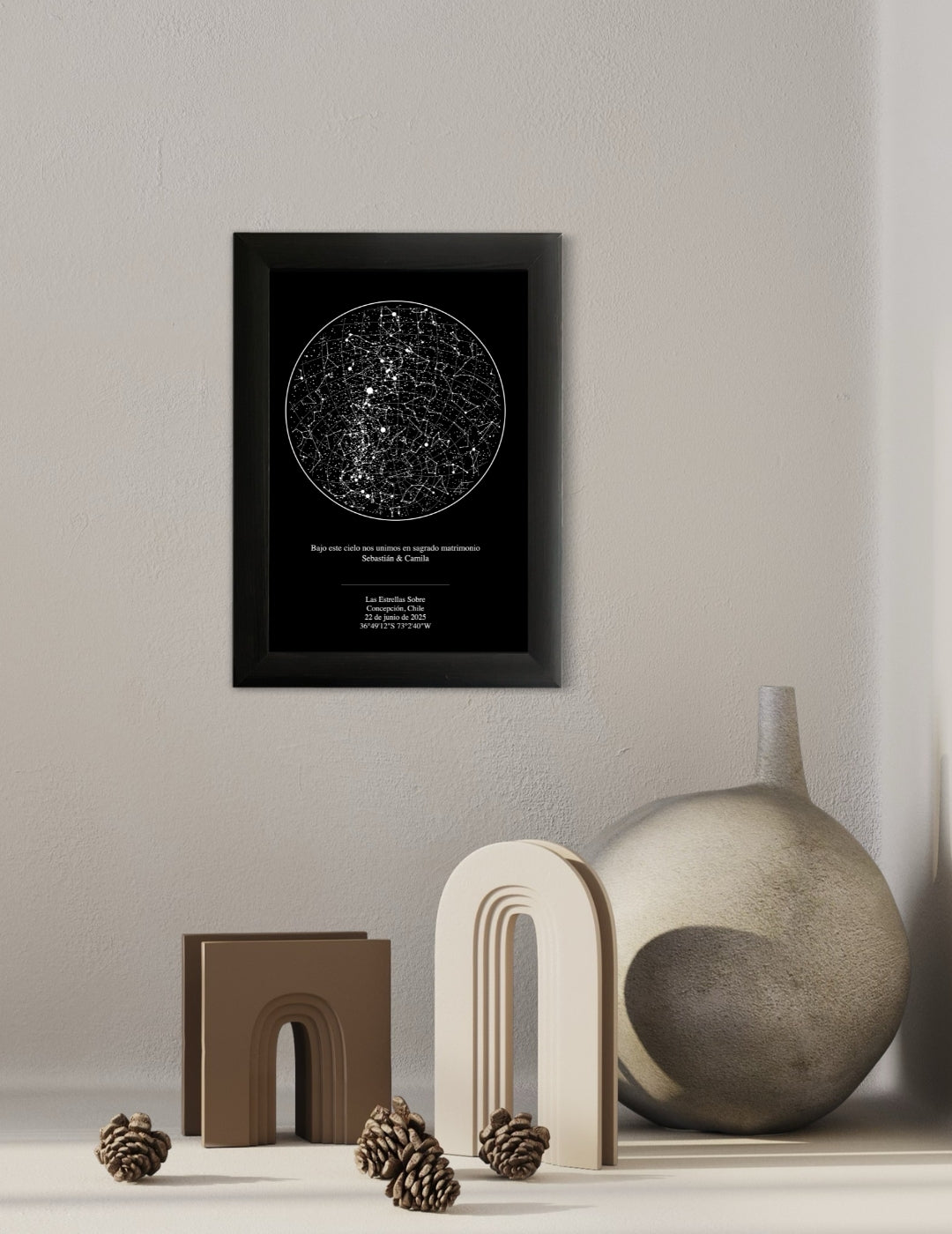Mapa estelar tradicional en marco negro colgado sobre una repisa decorada con esculturas beige, jarrón y piñas, ideal como regalo de boda elegante.