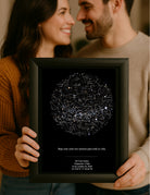 Pareja sonriendo mientras sostiene un Mapa Estelar Sky of Colors en marco negro, ideal como regalo de aniversario.