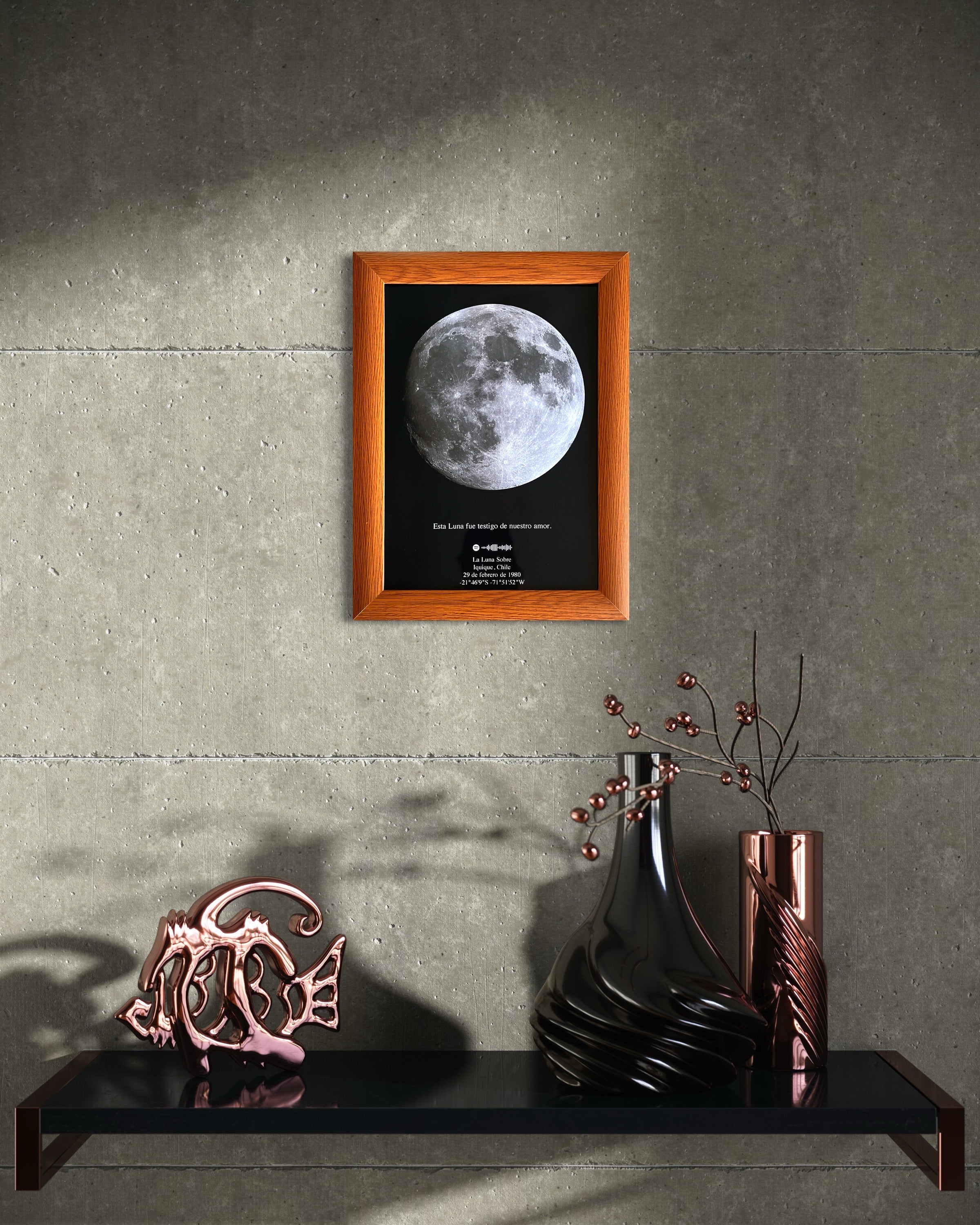 Cuadro con mapa lunar enmarcado en madera color miel sobre pared gris, decorando repisa moderna con jarrones y ramas secas. Ideal como regalo romántico y pieza de arte astronómica para el hogar.