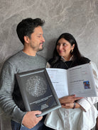 Pareja de pie mirando sus ojos mientras sostiene el Álbum para Parejas "Esto va en serio" abierto y un Mapa Estelar Sky of Colors enmarcado.