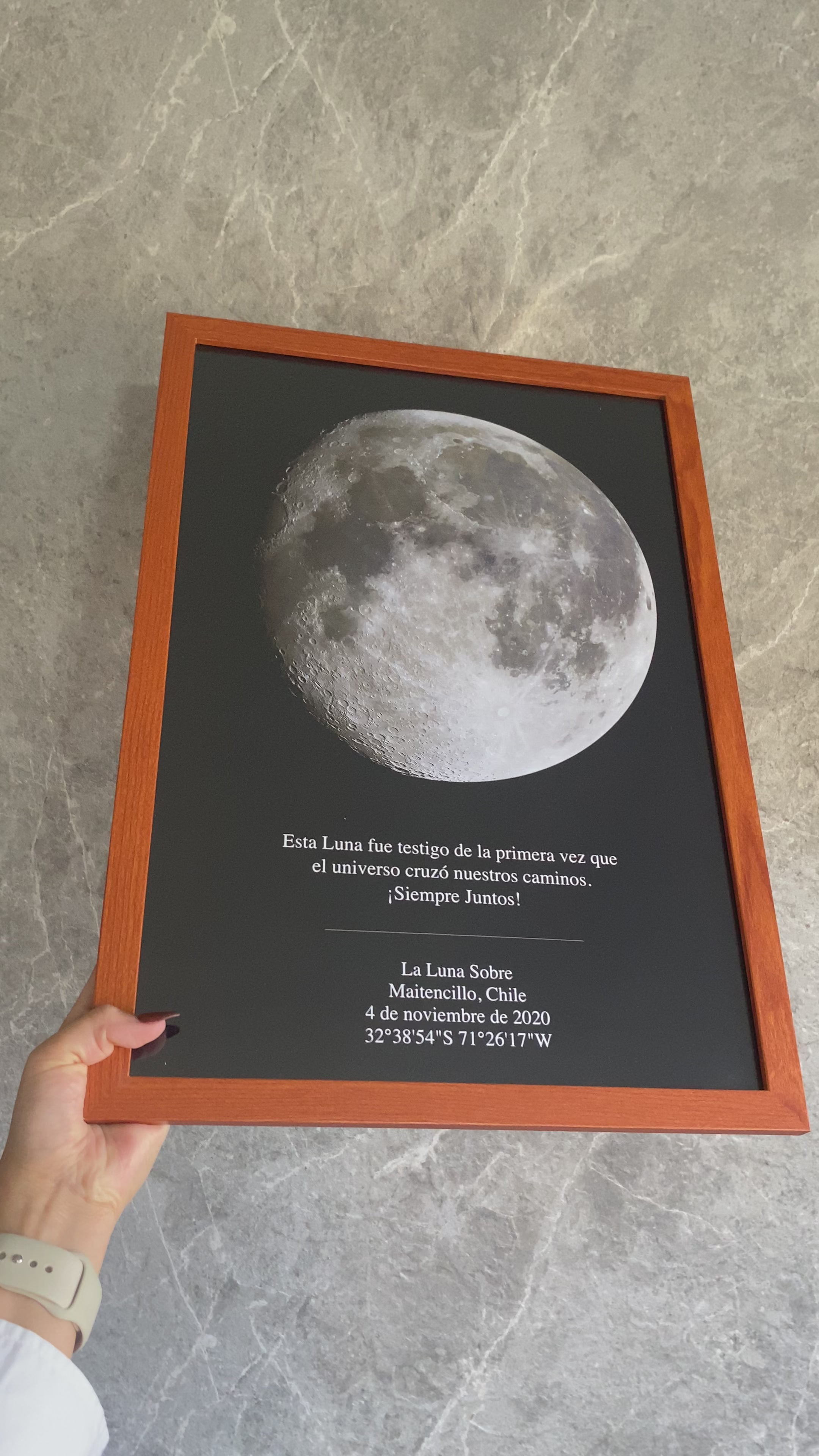 Mano sosteniendo cuadro Mapa Lunar XXL personalizado con fase exacta de la Luna, marco de madera y fondo gris, regalo romántico.