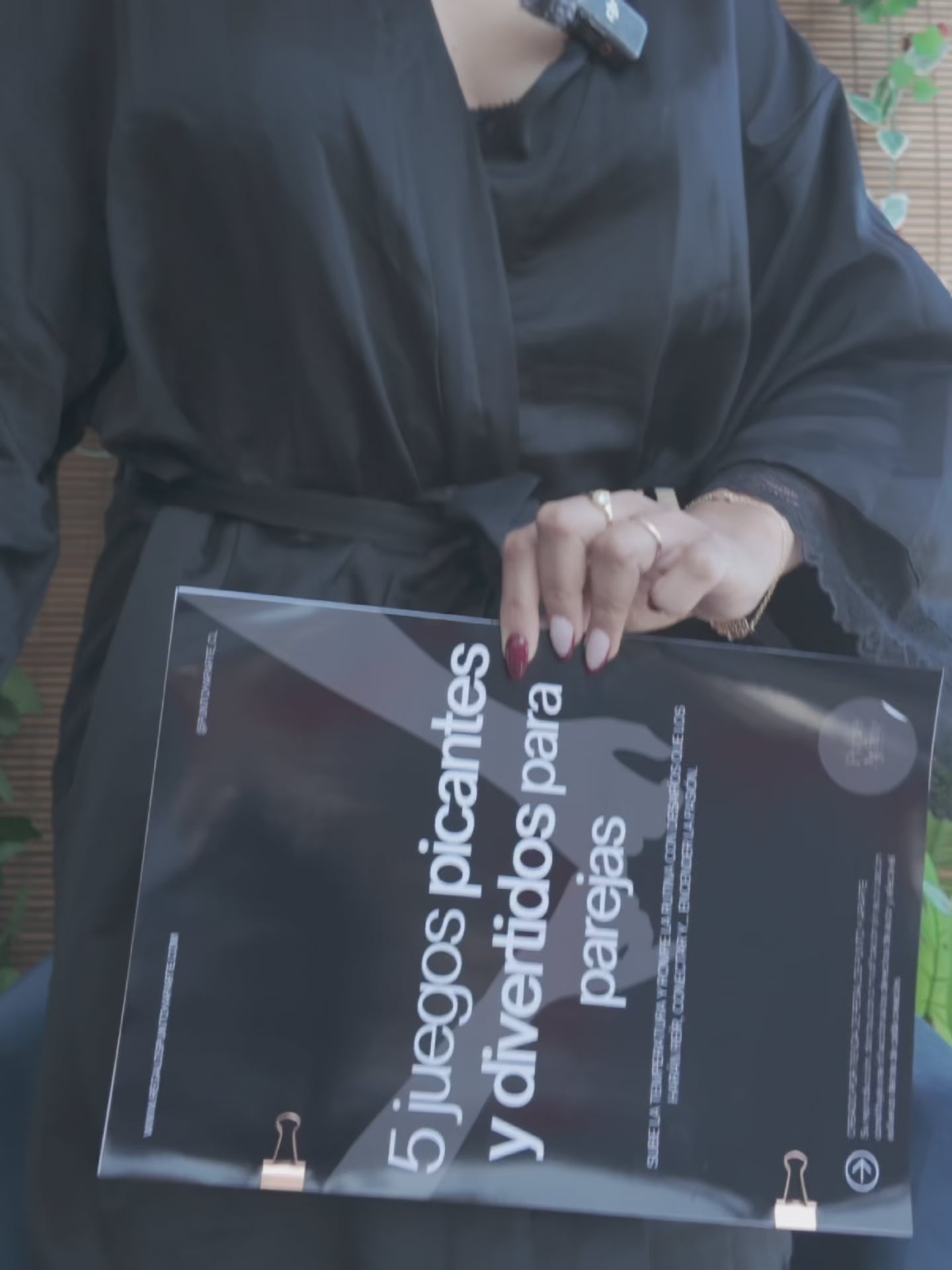 Video de una mujer en bata sosteniendo la revista 5 juegos picantes y divertidos para parejas en una terraza con plantas.