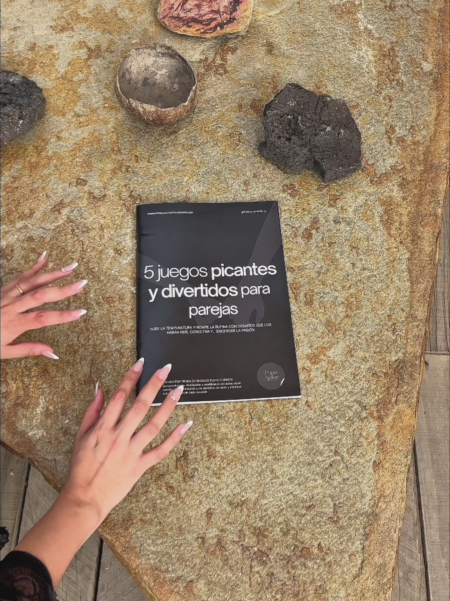 Video de la Revista 5 Juegos Picantes para parejas sobre una piedra, mostrando la portada en detalle y manos sosteniéndola.