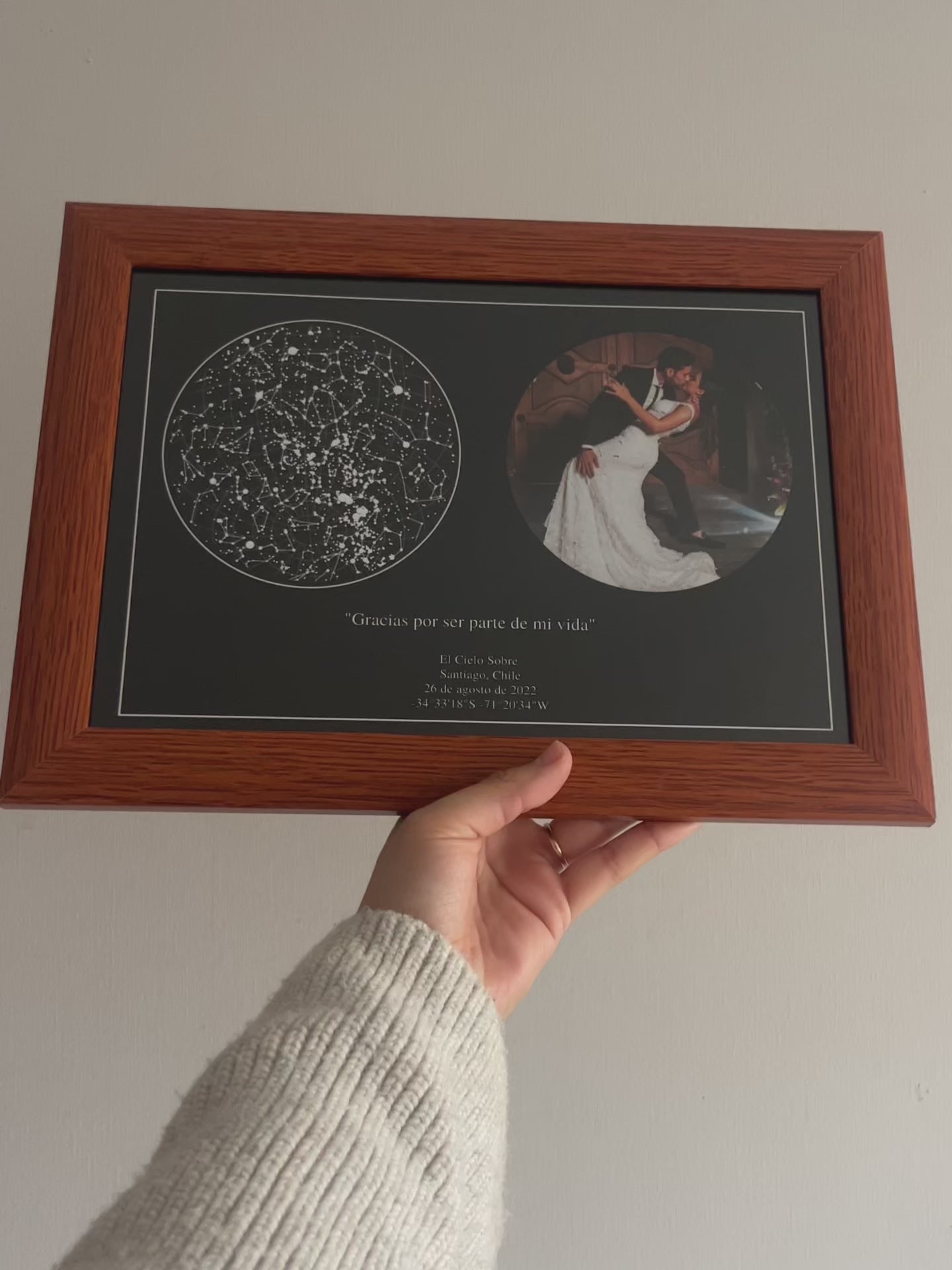 Mapa estelar Cielo Foto con cielo estrellado y foto de pareja en marco de madera, sostenido con la mano sobre pared clara.