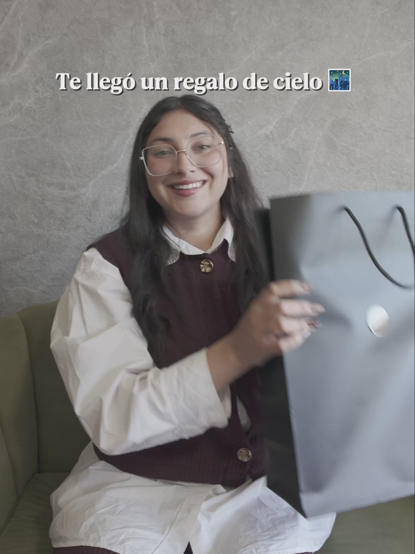 Video mujer sonriendo en un sillón mientras sostiene una bolsa de regalo de Punto & Aparte con un Mapa Estelar Sky of Colors en su interior.


