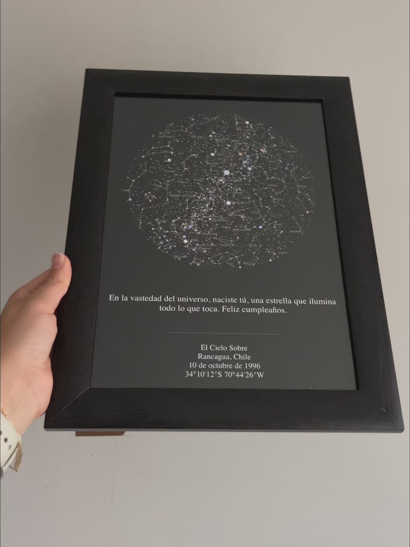 Video mostrando un Mapa Estelar Sky of Colors enmarcado en negro, sostenido con la mano, personalizado con fecha, ciudad y dedicatoria de cumpleaños.
